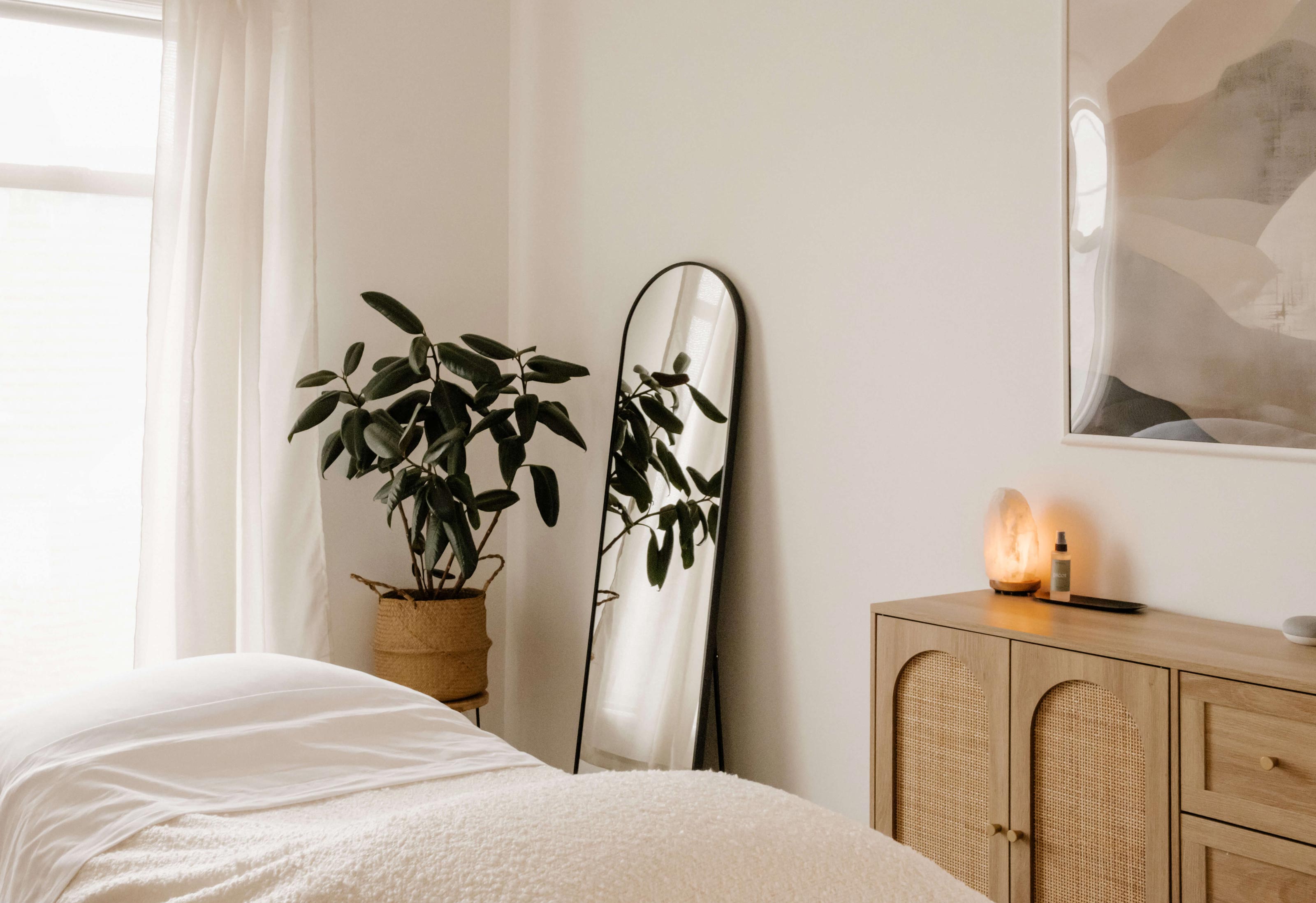 Interior photo of Opal Skin Studio treatment room with arched mirror, massage table, plan, and wooden side table with a salt lamp